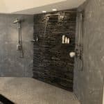 A shower with a textured tile floor and dark granite walls, showcasing the best tile for your shower remodel.