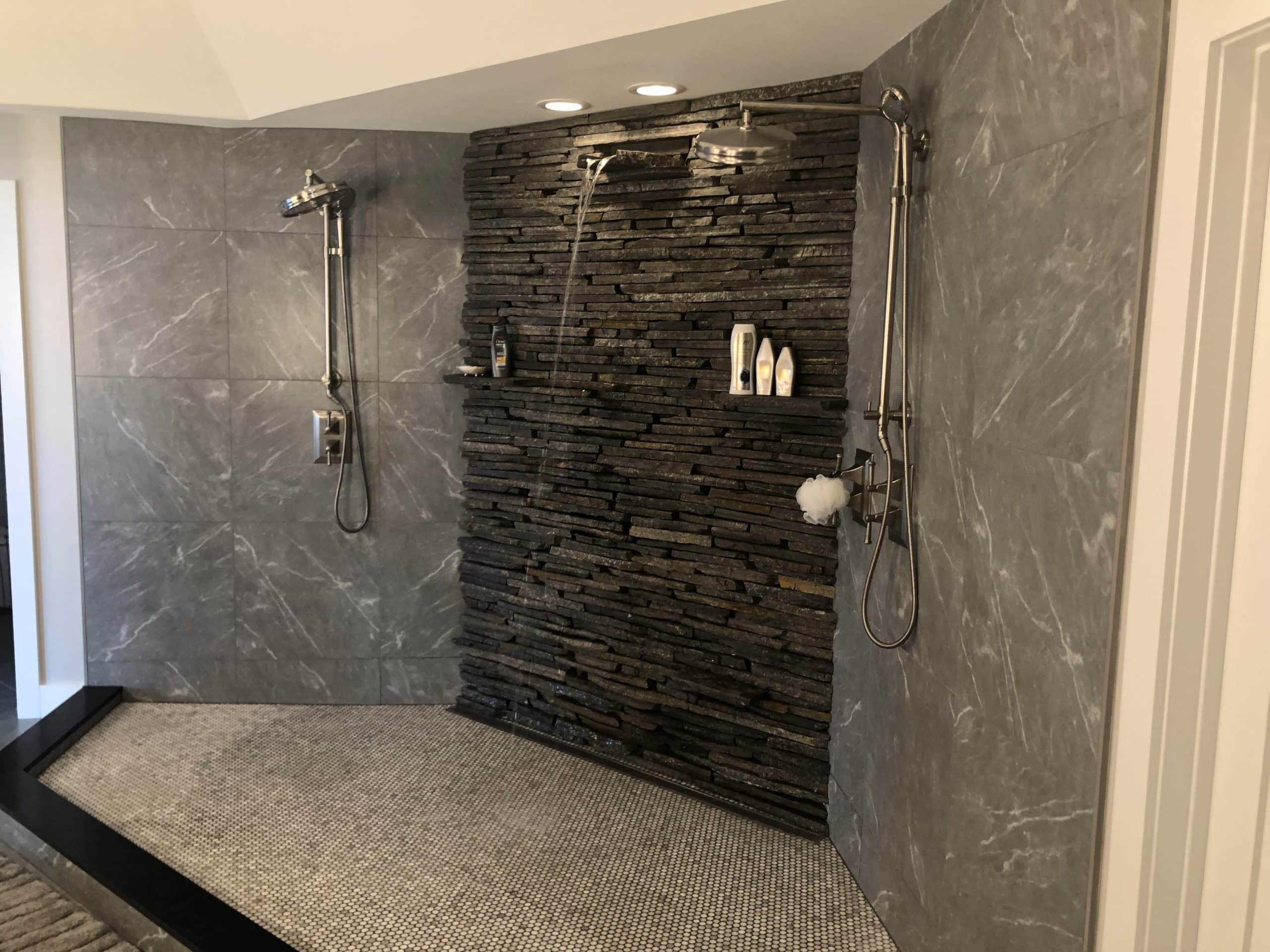 A shower with a textured tile floor and dark granite walls, showcasing the best tile for your shower remodel.