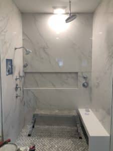 Tiled shower featuring a large rain shower head, additional handheld shower head, and a built-in bench. The floor showcases a contrasting herringbone tile pattern.