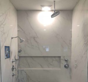 Tiled shower featuring a large rain shower head, additional handheld shower head, and a built-in bench. The floor showcases a contrasting herringbone tile pattern.