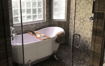 Freestanding bathtub with patterned tile walls, pebble flooring, and a glass-enclosed shower