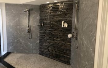 A shower with a textured tile floor and dark granite walls, showcasing the best tile for your shower remodel.